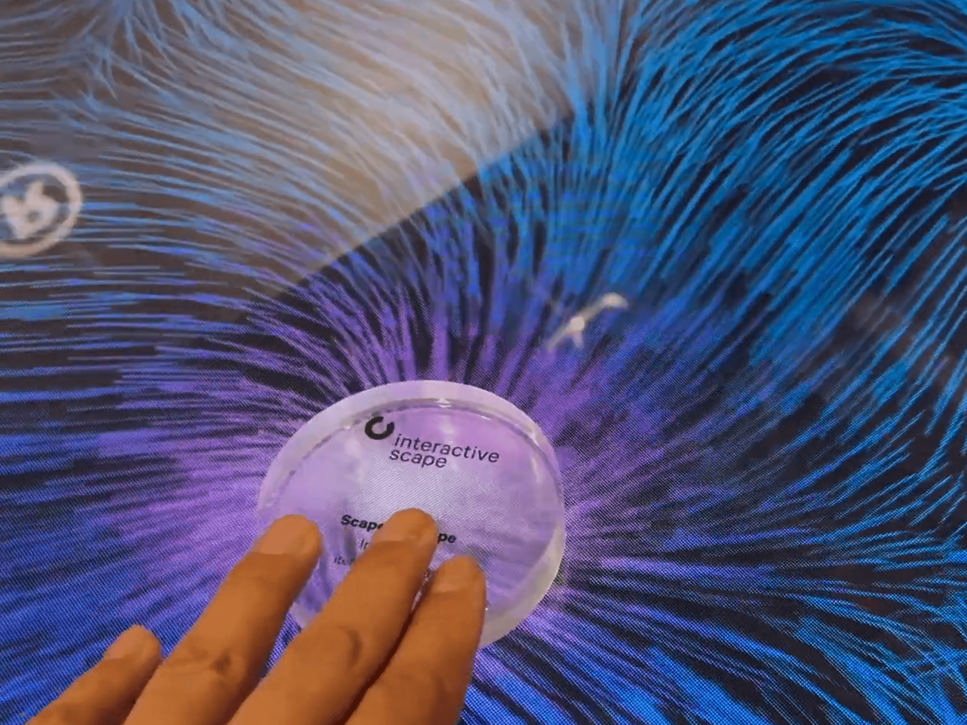 A translucent Scape X Sticker moves through a flowing particle visualization on the table