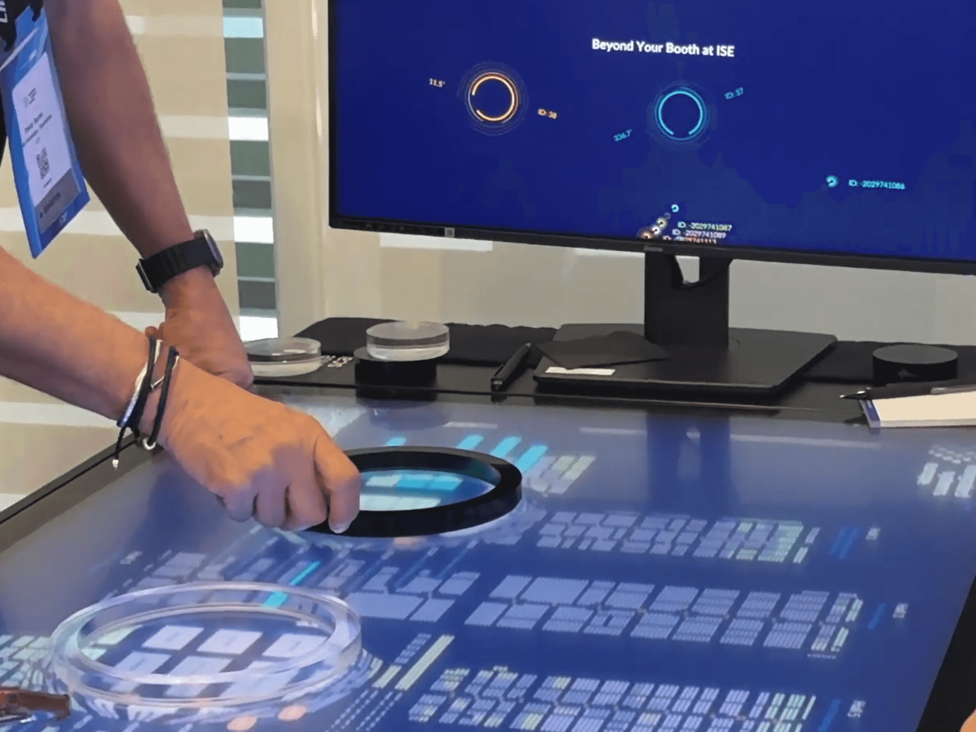 A visitor explores an interactive exhibition floor plan with tangible objects while recognized IDs appear on a monitor